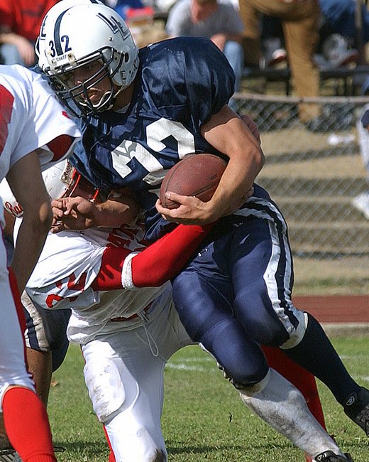 A youth football running back carrying the ball through contact.
